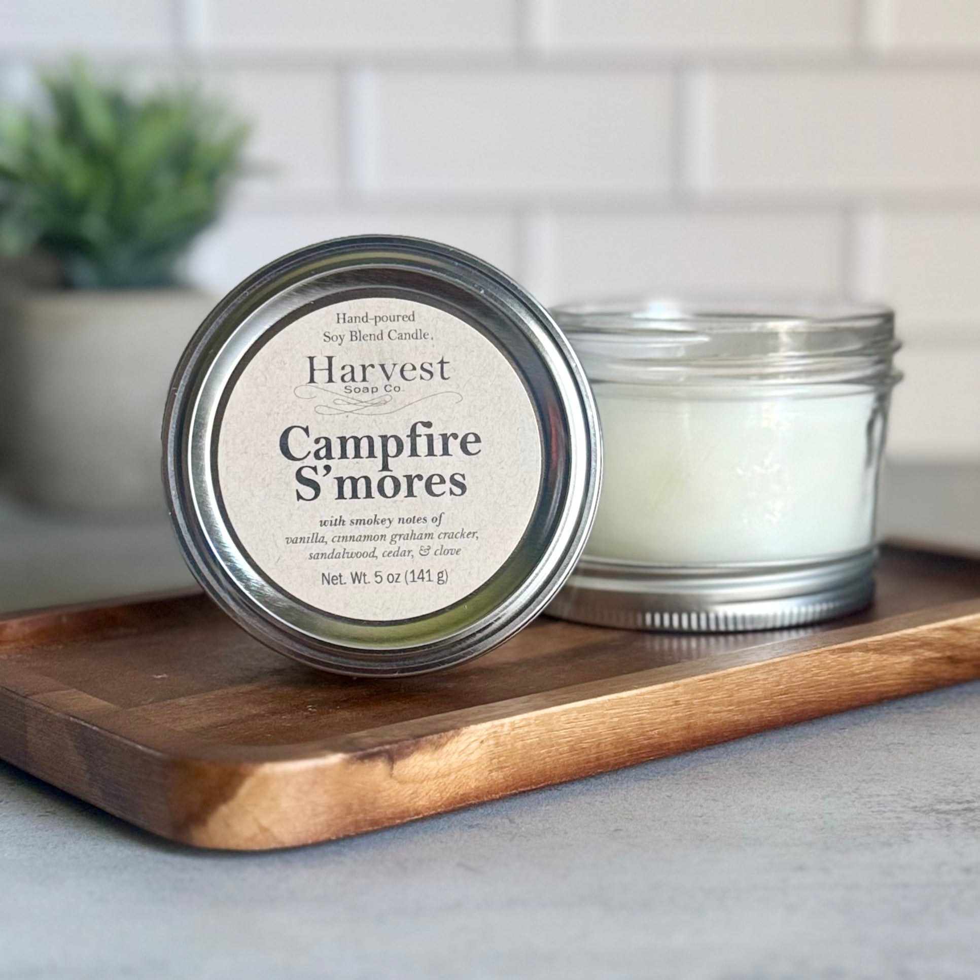 Harvest Soap Company Campfire S’mores Candle burning with a cozy glow and visible marshmallow and graham cracker scent notes.