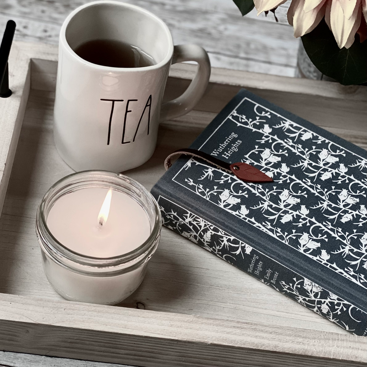 Lit candle in a tray with a cup of tee and a hardcover book