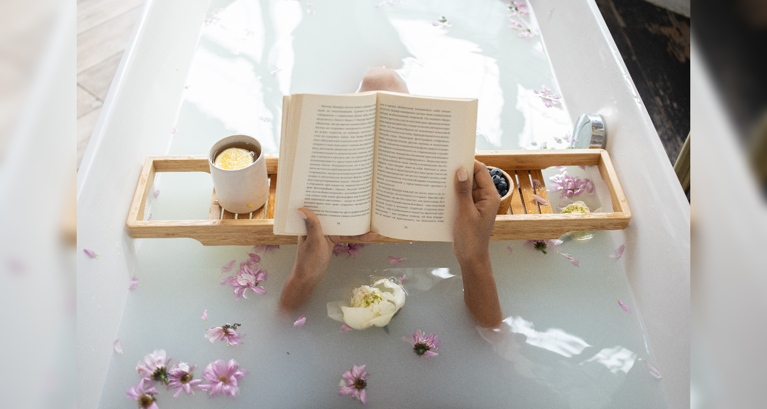 woman in a bath with flowers reading a book and drinking tea