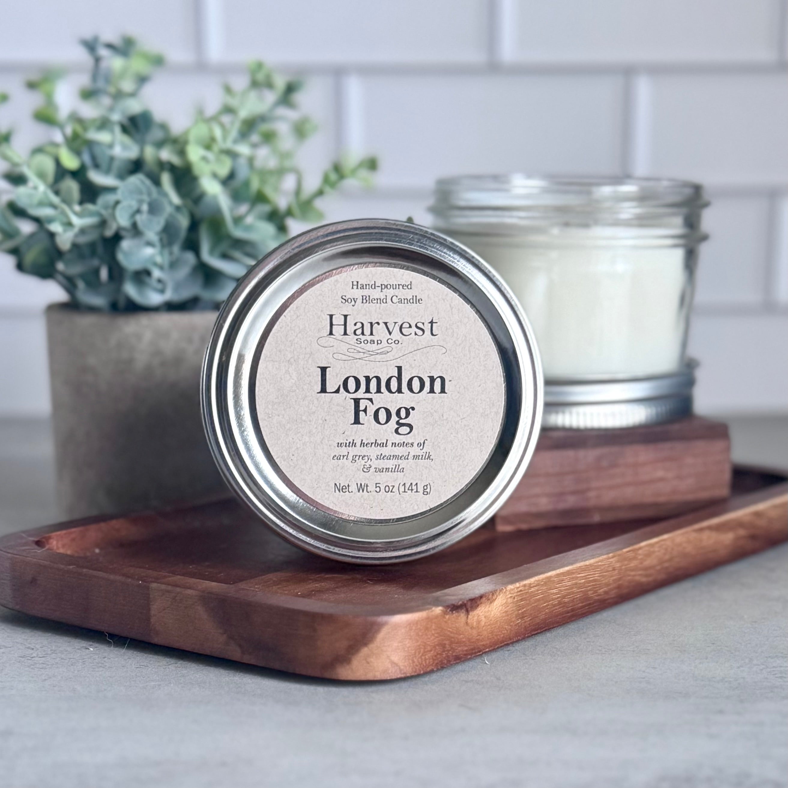 London Fog Candle by Harvest Soap Company with a sleek glass jar and a lit wick, emitting warm ambient light.
